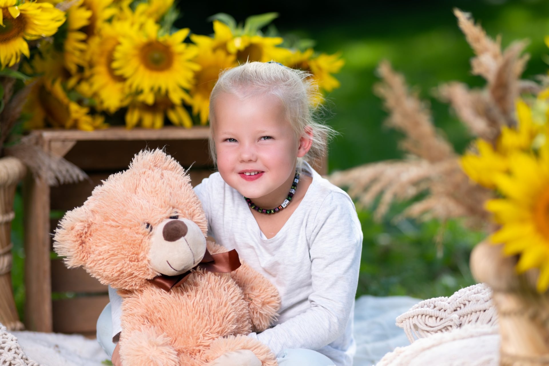 Kita-Kind hält lächelnd einen Teddybären vor Sonnenblumen