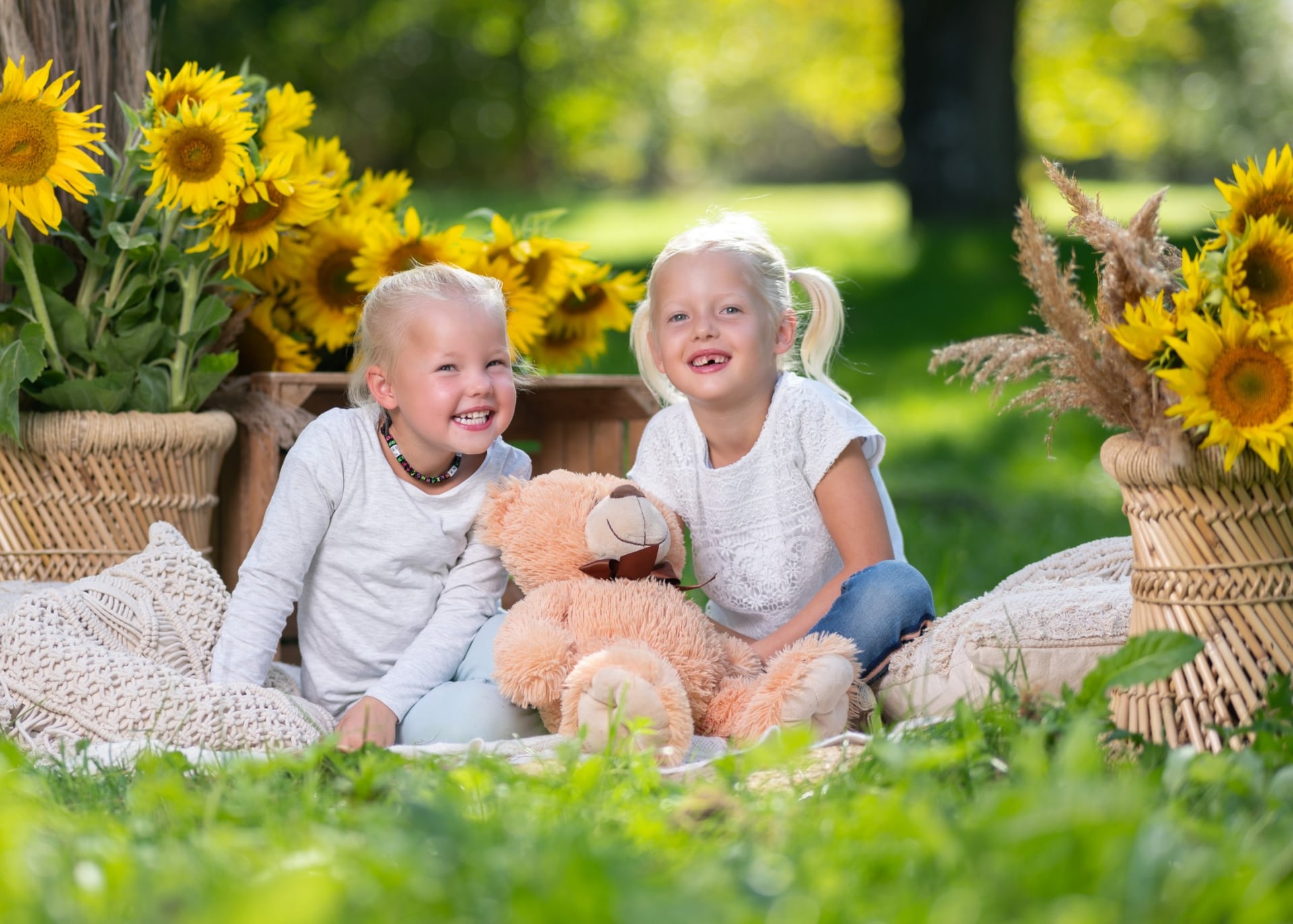 Zwei Schwestern lachen mit einem Teddybären auf einer Picknickdecke