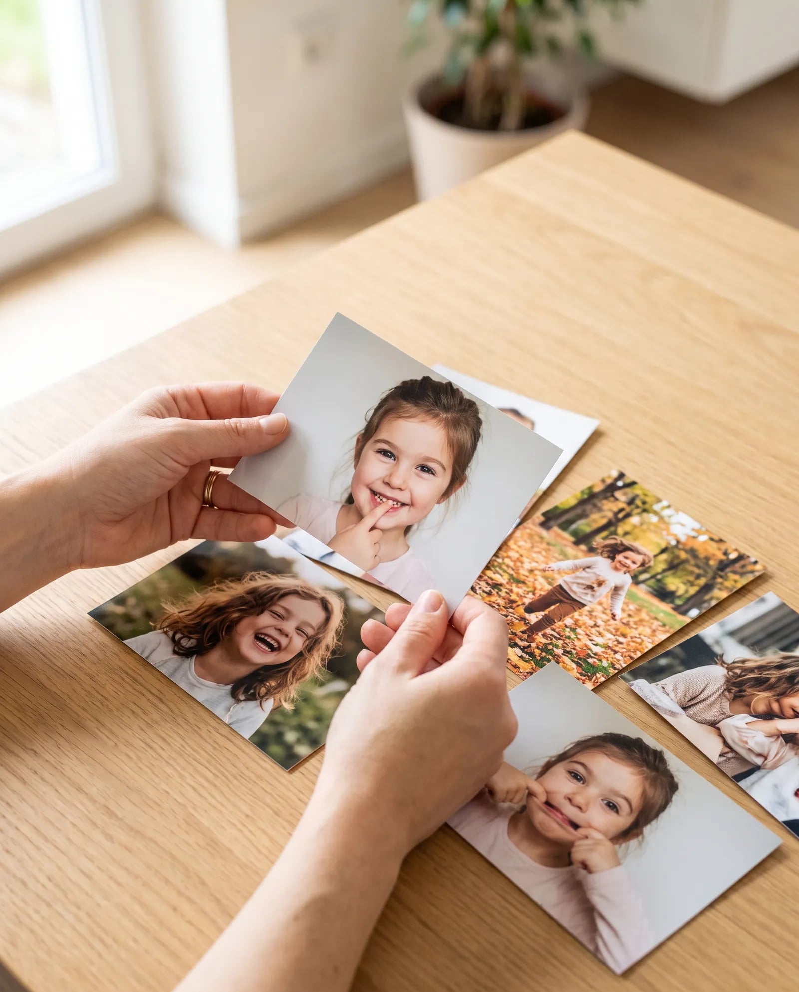 Hand hält gedruckte Kinderfotos über einem Holztisch